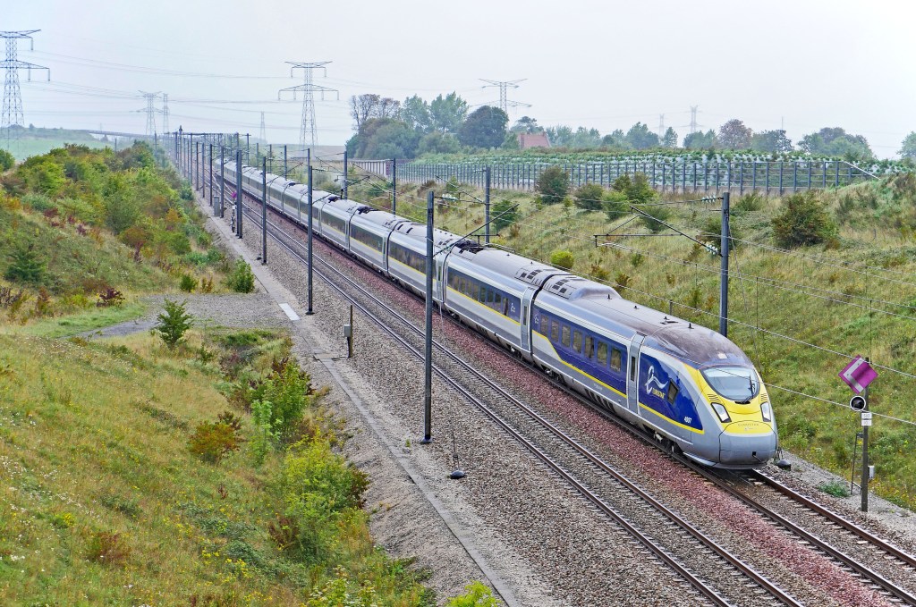 A high-speed EuroStar train traveling along railway tracks through a grassy landscape under a cloudy sky.