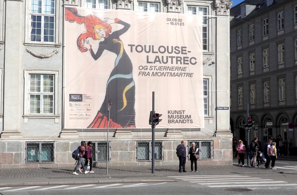 A large banner featuring a colorful illustration of a woman promoting a Toulouse-Lautrec exhibition at Kunst Museum Brandts in Copenhagen.