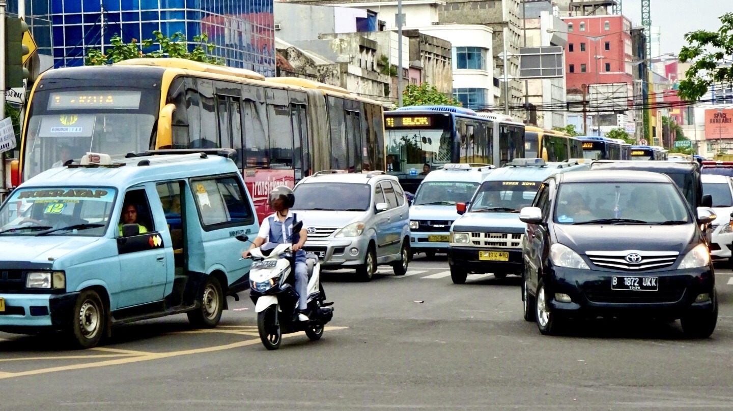 This image shows typical traffic conditions in Jakarta, Indonesia. A broken down van is blocking one of the traffic lanes, buses are queuing back into the distance on the adjacent busway and general traffic is at a standstill. This is a dual three lane highway (plus the central busway) linking northern Jakarta to the central area. It is included here to set the scene regarding typical driving conditions in Southeast Asia
