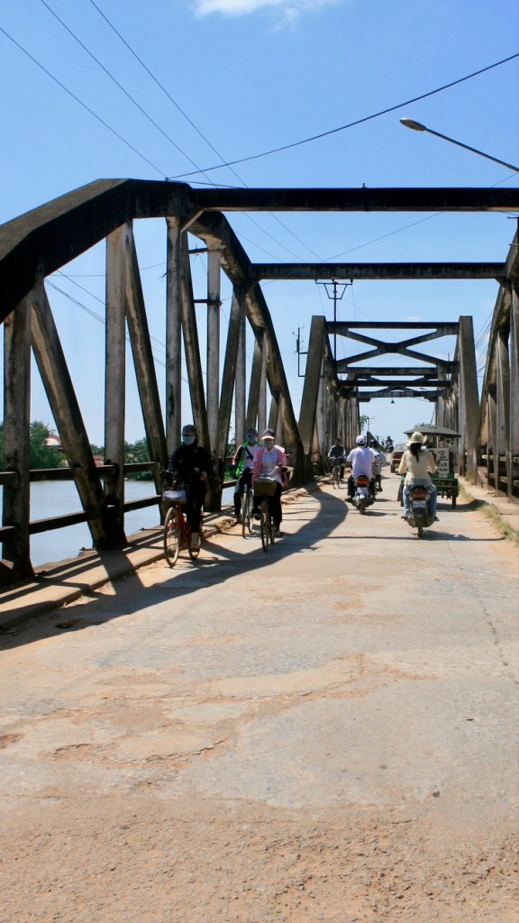 The photo shows an iron girder bridge crossing the Preaek Tuek Chhu in Kampot, Cambodia