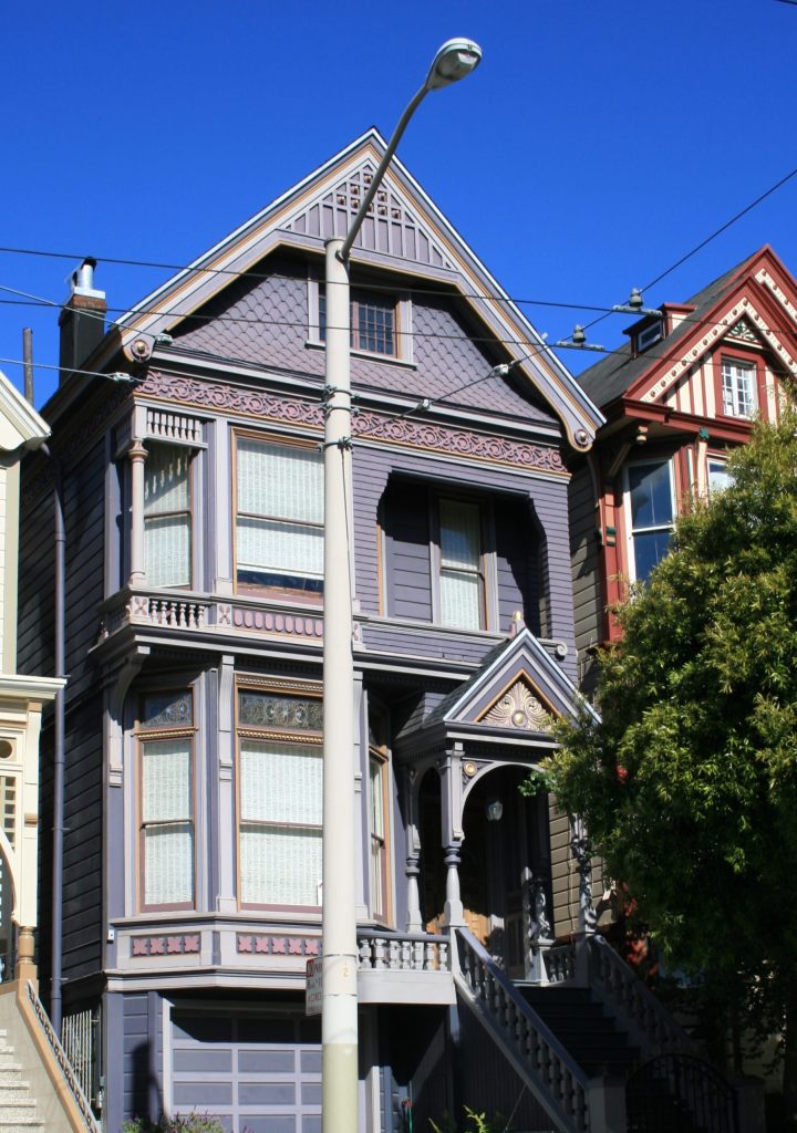 This image shows the Grateful Dead House at No 710 Ashbury Street, Haight-Ashbury, San Francisco, California. The house. which is painted in a purple colour, is a vintage Queen Anne Victorian building providing a basement, two full floors above and an attic, all under a gabled roof.  At ground floor the building has an arch porched door and bay window, while at first floor there is a balcony and another bay window. The house was home to members of the Grateful Dead rock group in the late 1960's and during the 1967 Summer of Love.