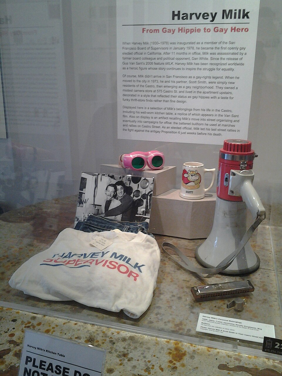 This image shows the contents of a display cabinet at the GLBT Historical Society Museum, Castro, San Francisco. The display cabinet contains the personal belongings of Harvey Milk, a GLTB activist in the 1970's. The possessions shown in the picture include a megaphone, cup, mouth organ, personalised bag and personal photographs. The cabinet in the photograph also includes a display board explaining the relevance of Harvey Milk to the story of the GLTB movement in Castro. He was a campaigner who became the first gay person to be elected to the City's Board of Governors. Shortly after his election he was assassinated by a former member of the Board.