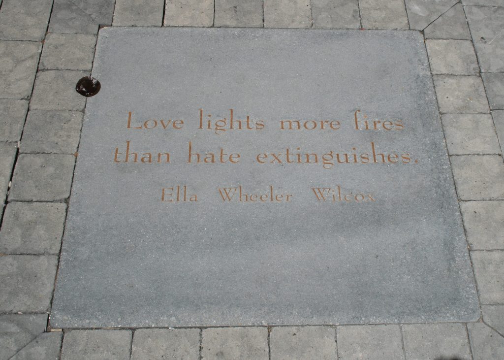 This image shows a pavement plaque carrying the words ' Love lights more fires than hate extinguishes'. Below the quotation is the name 'Ella Wheeler Wilcox'