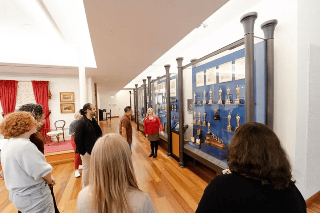 This image shows an interior gallery within the Walt Disney Family Museum. In the picture a number of people are looking at a series of vertically mounted display cabinets exhibiting various Walt Disney related artefacts.